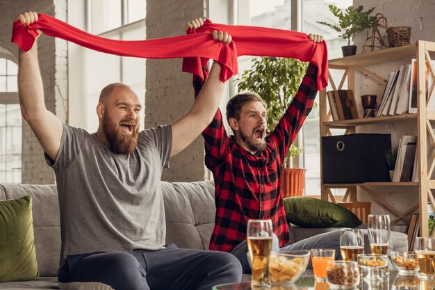 Victory. Excited, happy friends watching basketball, football, soccer, tennis match, championship on the couch at home. Fans emotional cheering for favourite national team. Sport, TV, having fun.