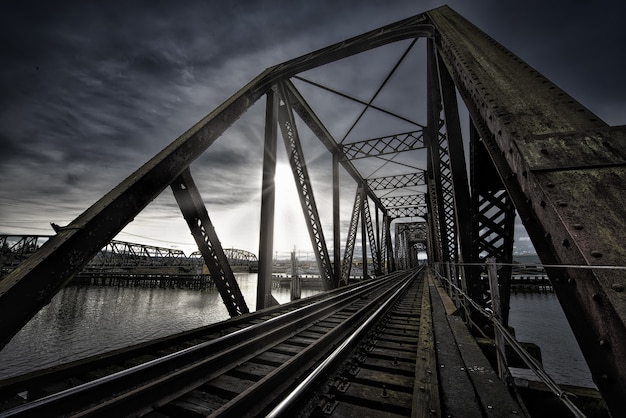 Free photo vierendeel bridge with train track near the lake and the breathtaking sun shining in the dark sky