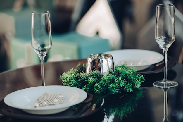 Free Photo view over beautifully decorated round table with natural fir branch, candle, two flutes, plates against classic sofa in modern apartment.