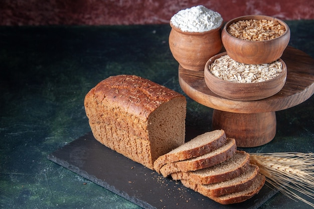 Free photo above view of black bread slices flour oatmeal buckwheat on dark color board on mixed color distressed background