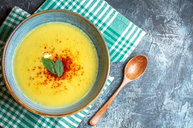 Above view of a blue pot with tasty soup served with mint and wooden spoon on green stripped towel on blue background