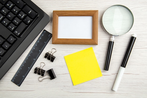 Free photo above view of brown empty picture frame and half shot laptop ruler marker magnifying glass paper clips on white stripped