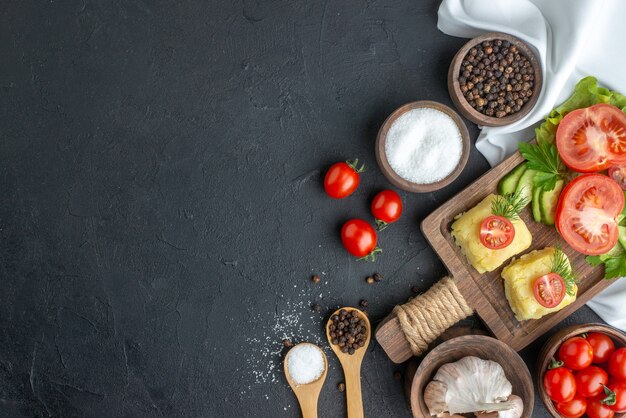 Above view of chopped and whole fresh vegetables on cutting board in bowls and spices on white towel on black surface