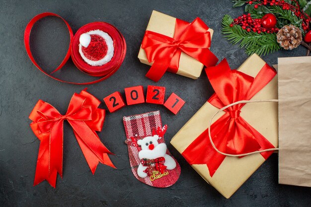 Above view of Christmas mood with beautiful gifts fir branches conifer cone red ribbon and numbers santa claus hat xsmas sock on dark background