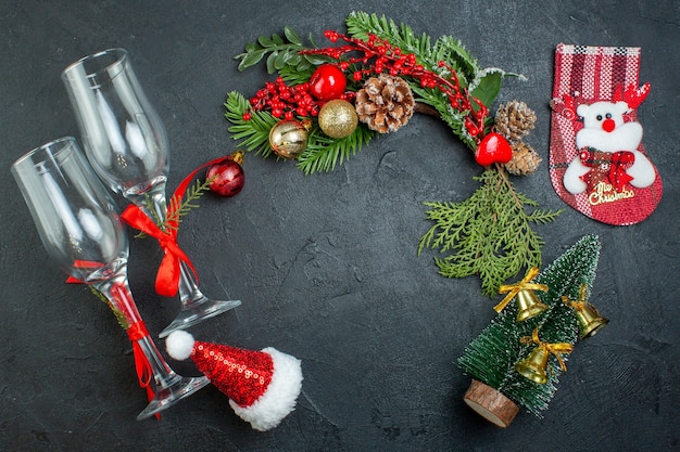 Above view of christmas mood with fallen glass goblets fir branches xsmas tree sock santa claus hat on dark background