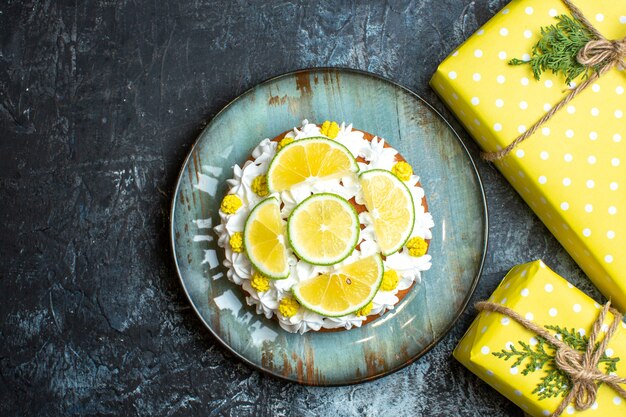 Above view of Christmas yellow gift boxes and cake decorated with lemon limes on dark background