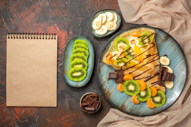 Free Photo above view of citrus fruits in delicious crepe decorated with chocolate sauce on a blue plate notebook on mixed color