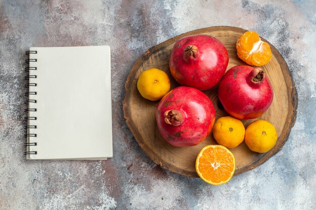 Above view of collection of fresh fruits with pomegranates oranges and tangerines on a wooden tray and notebook on ice background