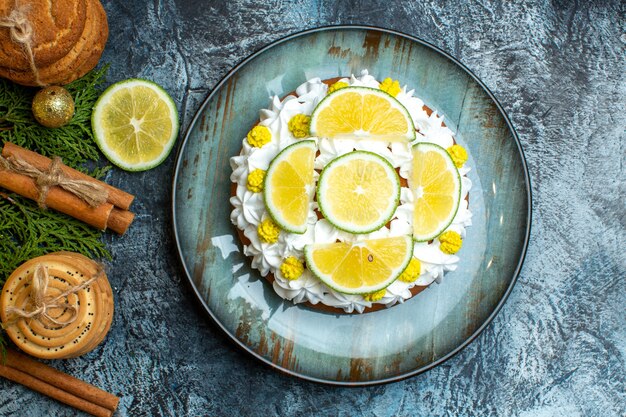 Above view of creamy delicious cake and fir branches lemon cinnamon limes on dark background