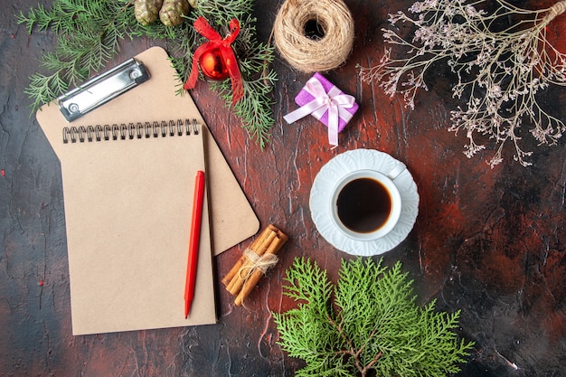 Above view of a cup of black tea fir branches cinnamon limes gift and notebook on dark background