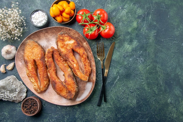 Free photo above view of delicious fried fish on a brown plate and cutlery set spices foods on mix colors table with free space