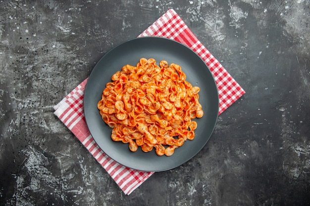 Free photo above view of delicious pasta meal on a black plate for dinner on a red stripped towel on dark background