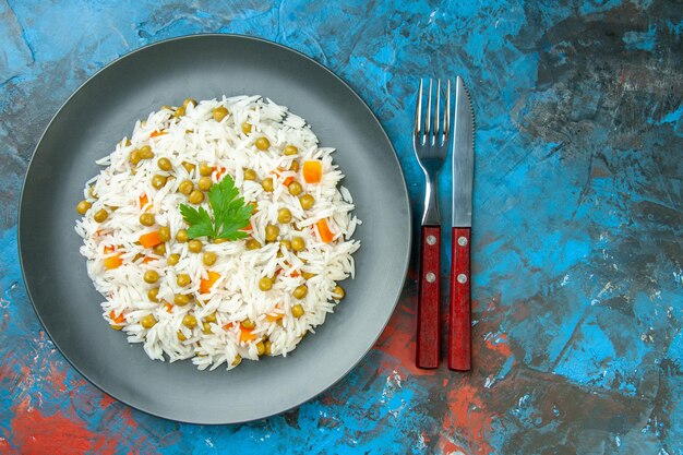 Above view of delicious rice meal with pisum carrot served with green on a plate cutlery set on mixed color background with free space