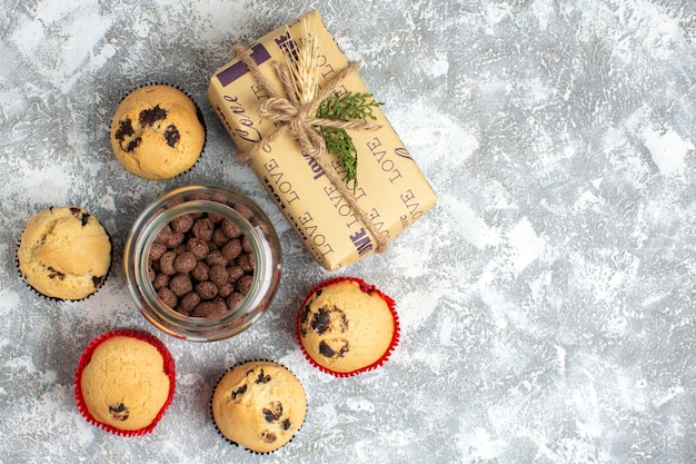 Free Photo above view of delicious small cupcakes and chocolate in a glass pot next to christmas gift on the right side on ice surface