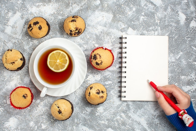 Free photo above view of delicious small cupcakes with chocolate around a cup of black tea and hand writing on notebook on ice surface