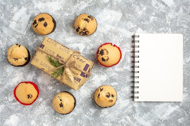 Above view of delicious small cupcakes with chocolate around gift with love inscription and notebook on ice surface