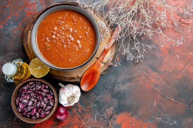 Above view of delicious soup for dinner with a spoon and lemon on a wooden tray beans garic onion and oil bottle on mixed color table