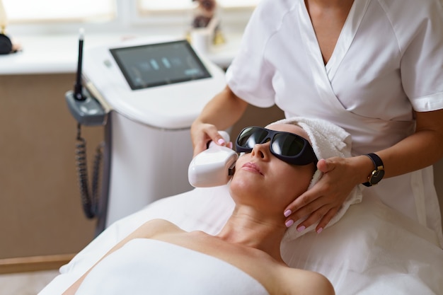 Free photo view of doctor cosmetologist doing anti aging procedure in cosmetology office. satisfied woman in disposable hat lying on couch and relaxing.