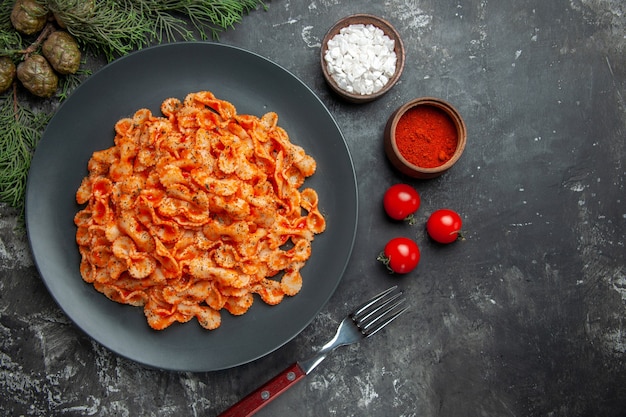 Free photo above view of easy pasta meal for dinner on a black plate and fork on different spices and tomatoes on a dark background