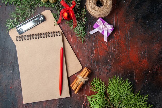 Above view of fir branches cinnamon limes gift and notebook on dark background