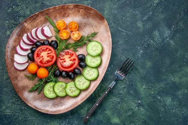 Free photo above view of fresh chopped vegetables olives in a brown plate and fork on green black mixed colors table