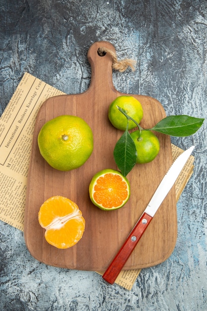 Free Photo above view of fresh citrus fruits with leaves on wooden cutting board cut in half forms and knife on newspaper on gray background