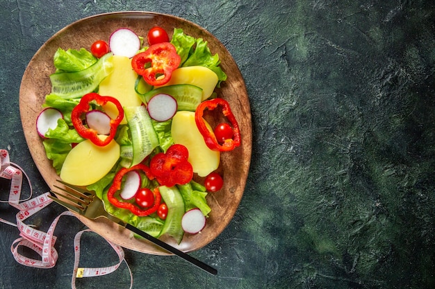 Free photo above view of fresh peeled cut potatoes with red pepper radishes green tomatoes fork in a brown plate and meters on green black mix colors surface