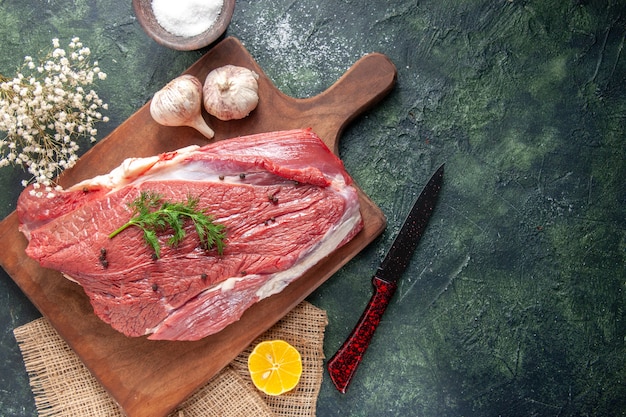 Above view of fresh raw red meat garlics on wooden cutting board lemon on nude color towel flower knife flour on mixed color background