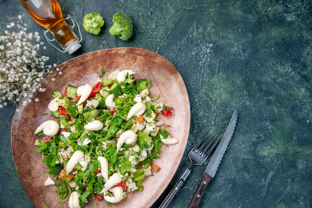 Free photo above view fresh vegetable salad inside elegant plate with cutlery on dark blue background