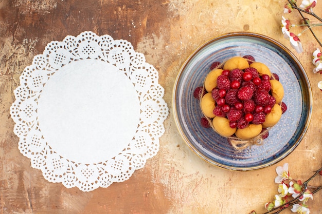 Free photo above view of freshly baked soft cake with fruits flowers and napkin on mixed color table