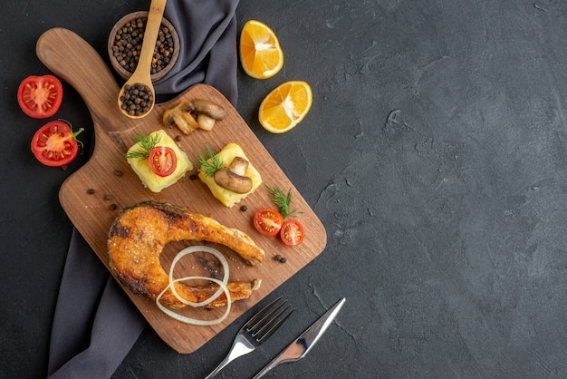 Free Photo above view of fried fish meal with mushrooms vegetables cheese on wooden board lemon slices pepper on dark color towel on the right side on black distressed surface