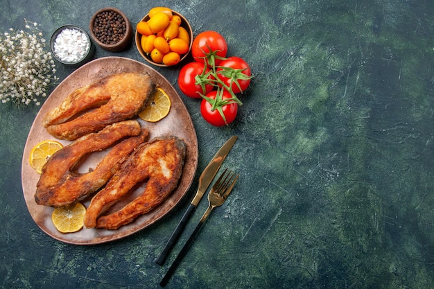 Free photo above view of fried fishes and lemon slices on a brown plate tomatoes kumquats on mix colors table with free space