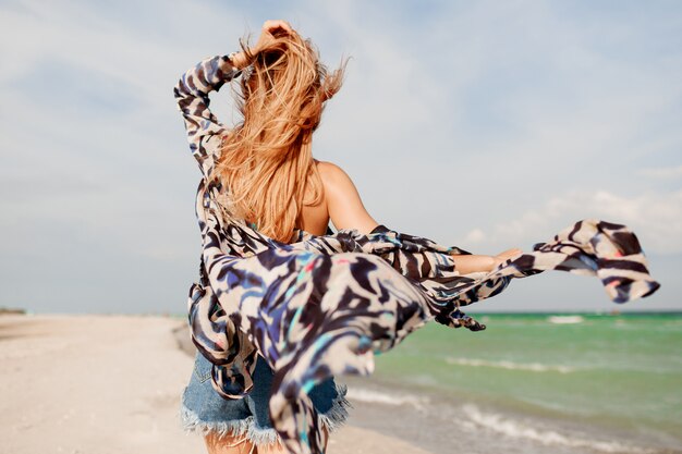 View from back of carefree graceful woman with amazing ginger hairs running along the beach