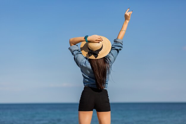 View from back. woman in straw hat, with figure looking on the sea.