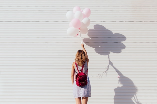 Free photo view from back of young woman with backpack, holding air balloons