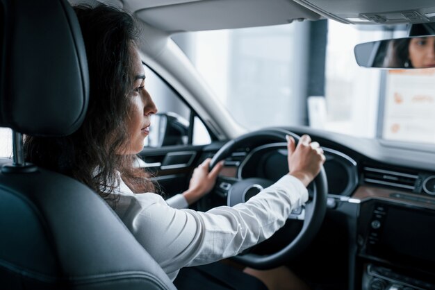 View from the inside. Beautiful businesswoman trying her new car in the automobile salon