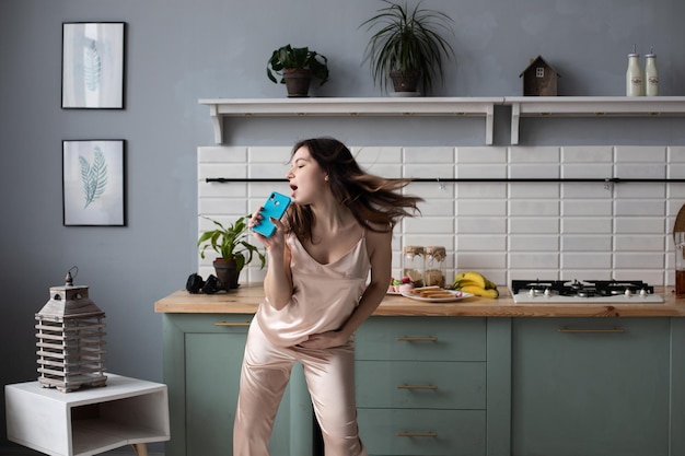 Free photo view from side of young girl wearing pajamas standing at kitchen and dancing in morning cheerful woman singing while preparing breakfast at home on weekends concept of preparation and happiness