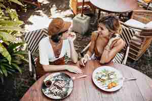 Free photo view from above at tanned womans in stylish outfits talking and enjoying tasty food in street cafe