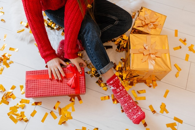 View from above on woman in red socks sitting at home at christmas on golden confetti unpacking peresents and gift boxes