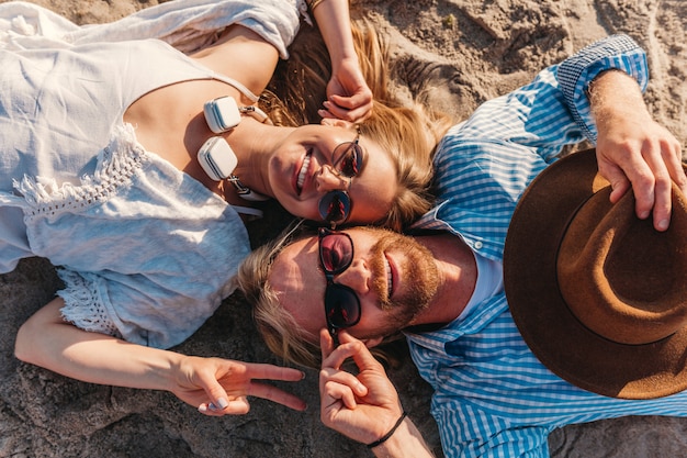 Free photo view from above on young smiling happy man and woman in sunglasses lying on sand beach