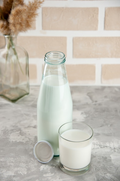 Above view of glass bottle and cup filled with milk cap on pastel color brick background