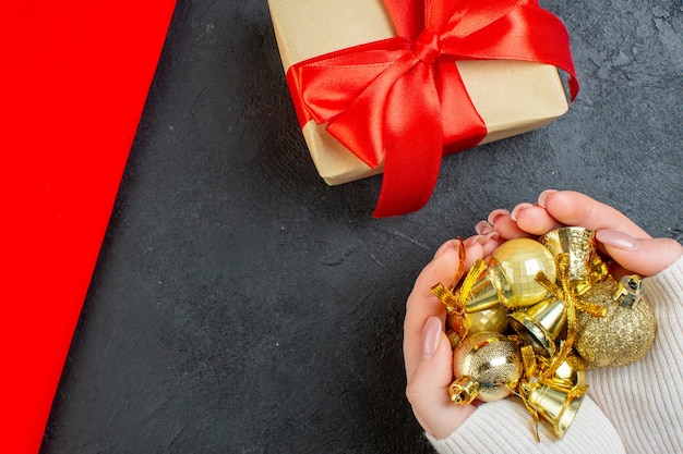 Free photo above view of hand holding colorful decoration accessories and beautiful gift on red towel on dark background