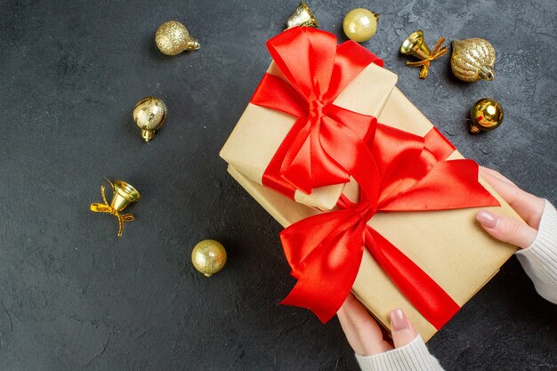 Above view of hand holding one of gift boxes with red ribbon and decoration accessories on dark background