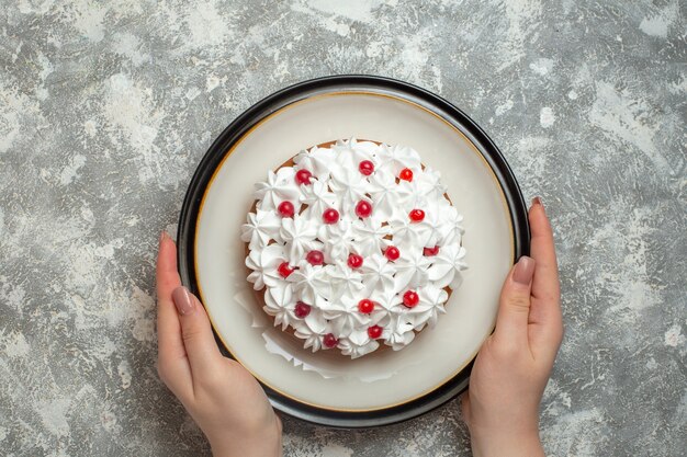 Above view of hand holding a plate with delicious creamy cake decorated with fruits on ice background