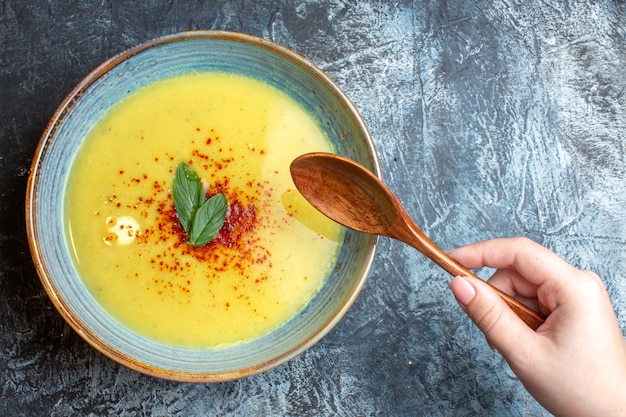 Free photo above view of hand holding a wooden spoon on tasty soup in a blue pot on blue background