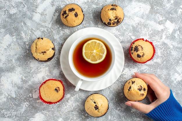 Free photo above view of hand taking one of delicious small cupcakes with chocolate on ice surface