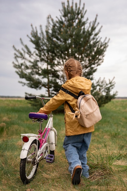 View of little girl with backpack and bike adventuring in nature