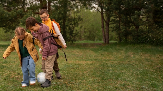 Free photo view of little kids with backpacks playing ball in nature