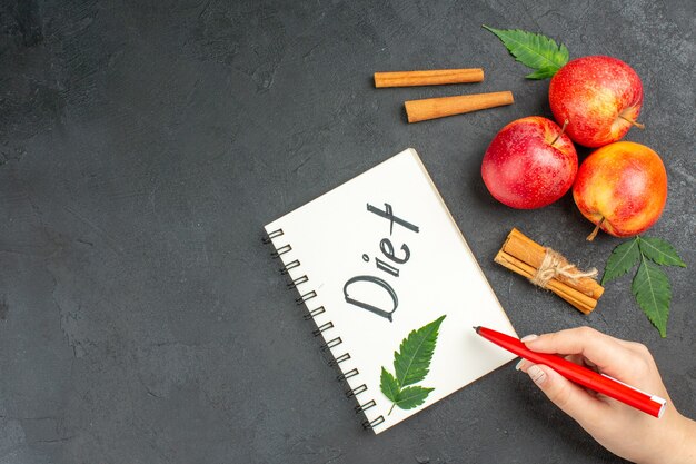 Above view of natural organic fresh apples with green leaves cinnamon limes notebook with diet inscription on black background