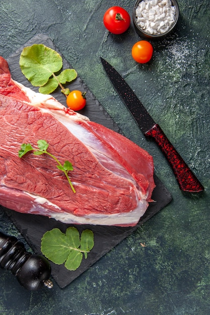 Free photo above view of raw fresh red meat and greens on cutting board knife tomatoes wooden hammer on green black mix colors background